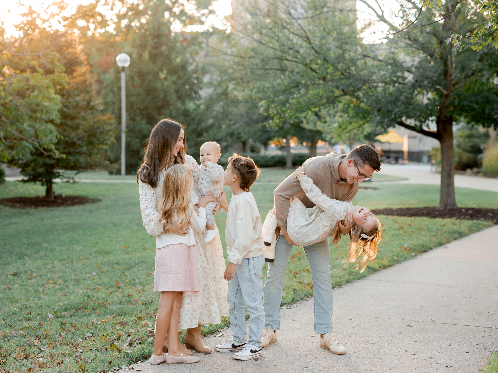 Dad dips his daughter while the Bedford family laughs together outdoors at sunset, captured by Columbia Missouri family photographer Love Tree Studios.
