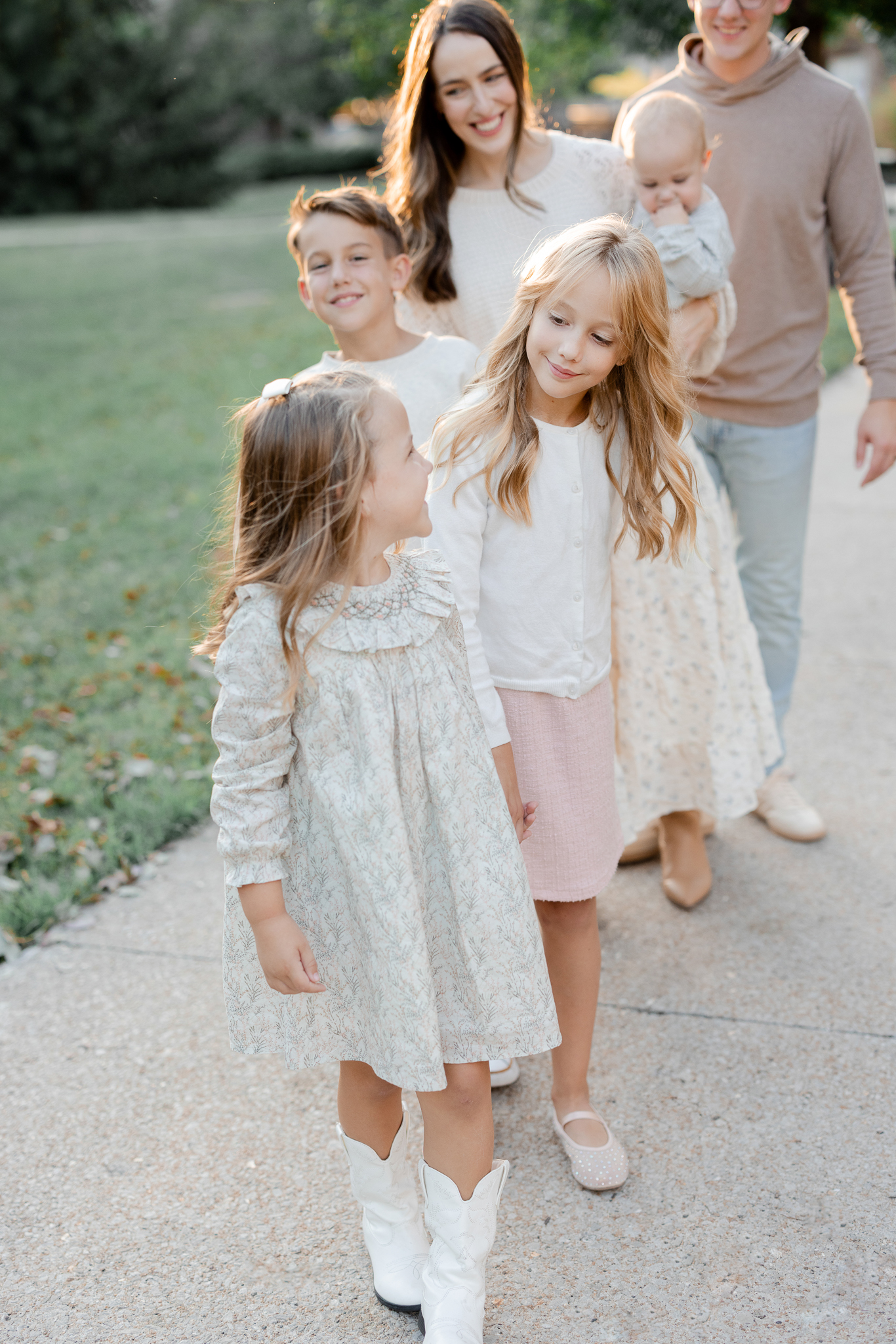 Sisters walk together in front while parents follow behind, Columbia Missouri family photographer capturing natural connection.