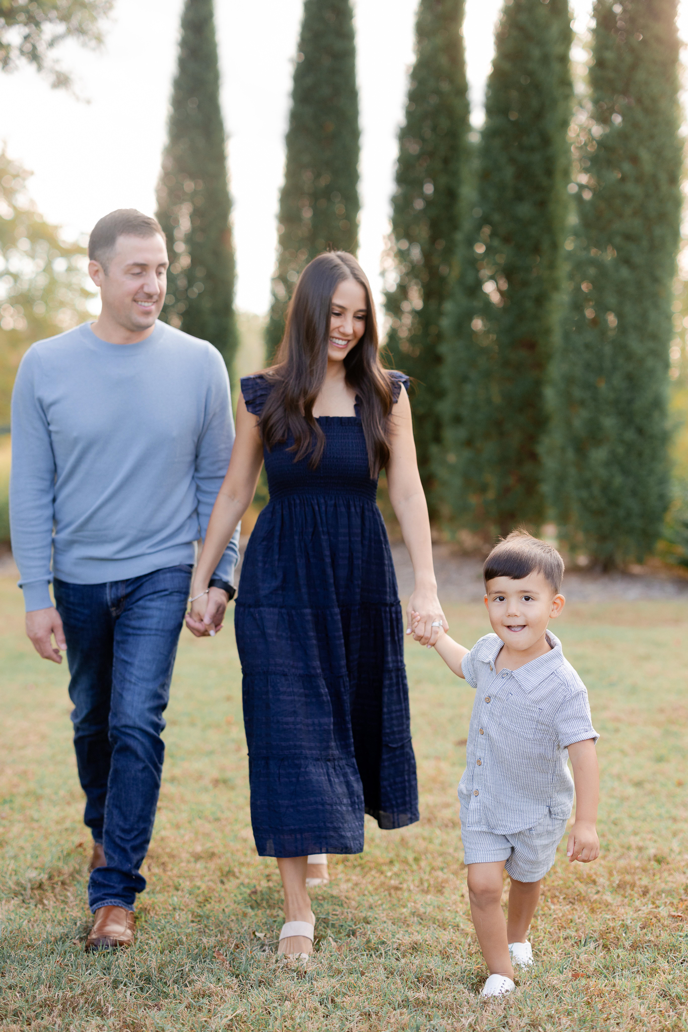 Little boy walking hand-in-hand with his parents, smiling brightly during a Columbia Missouri family session.