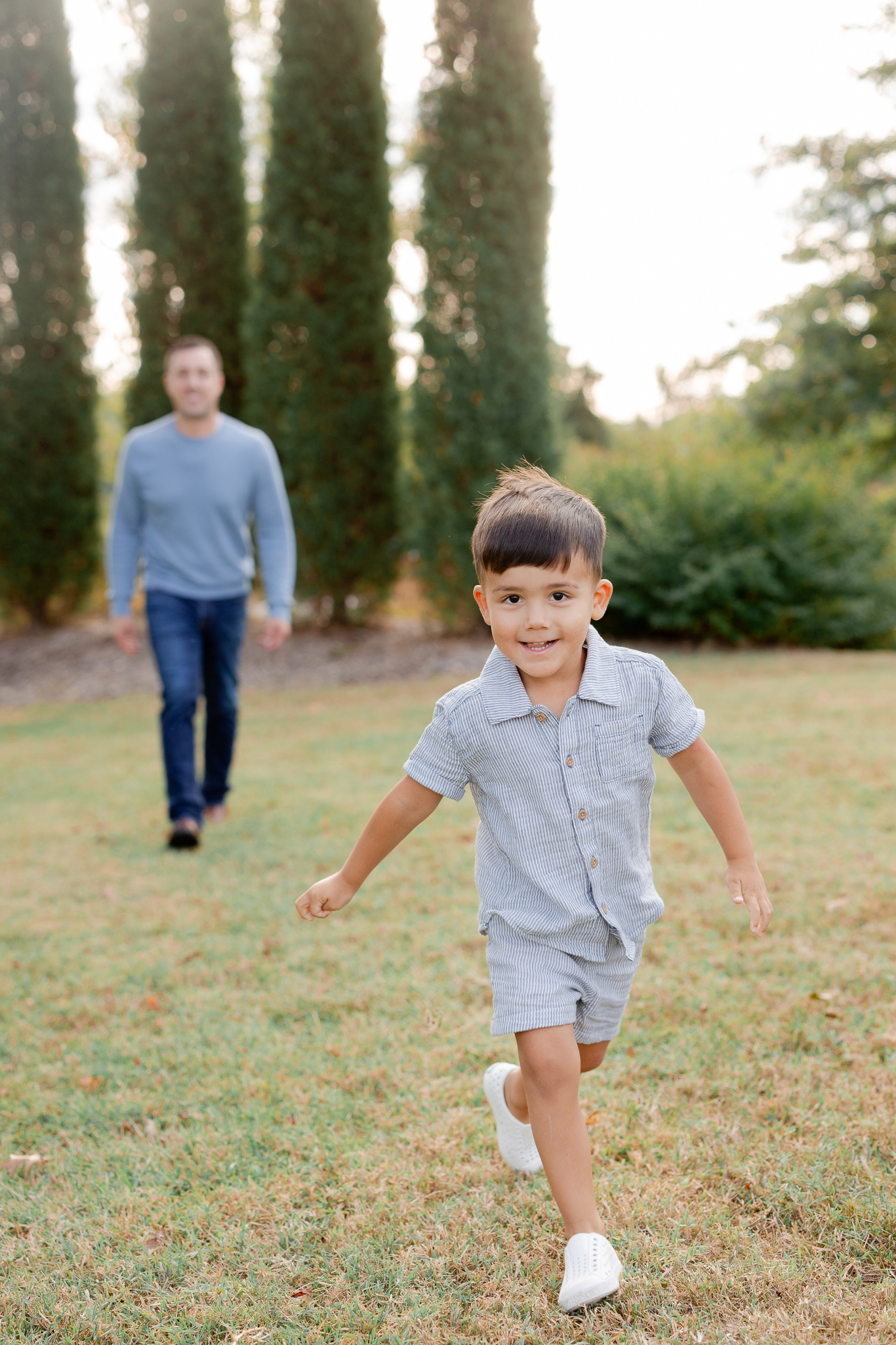Playful candid of young boy running while dad smiles in the background during a Love Tree Studios session.