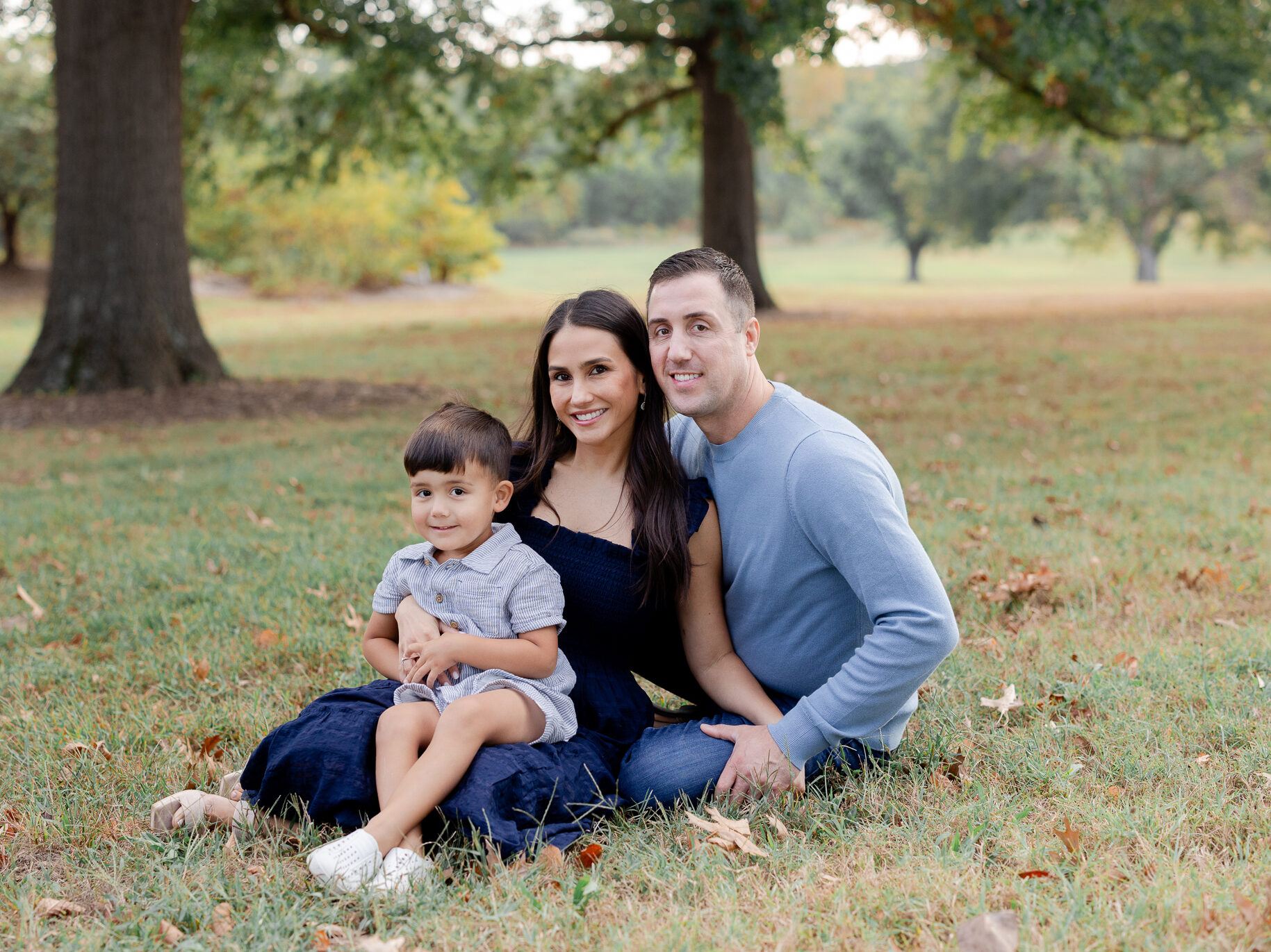 Family snuggled close together with golden backlight filtering through evergreens, captured by Love Tree Studios.