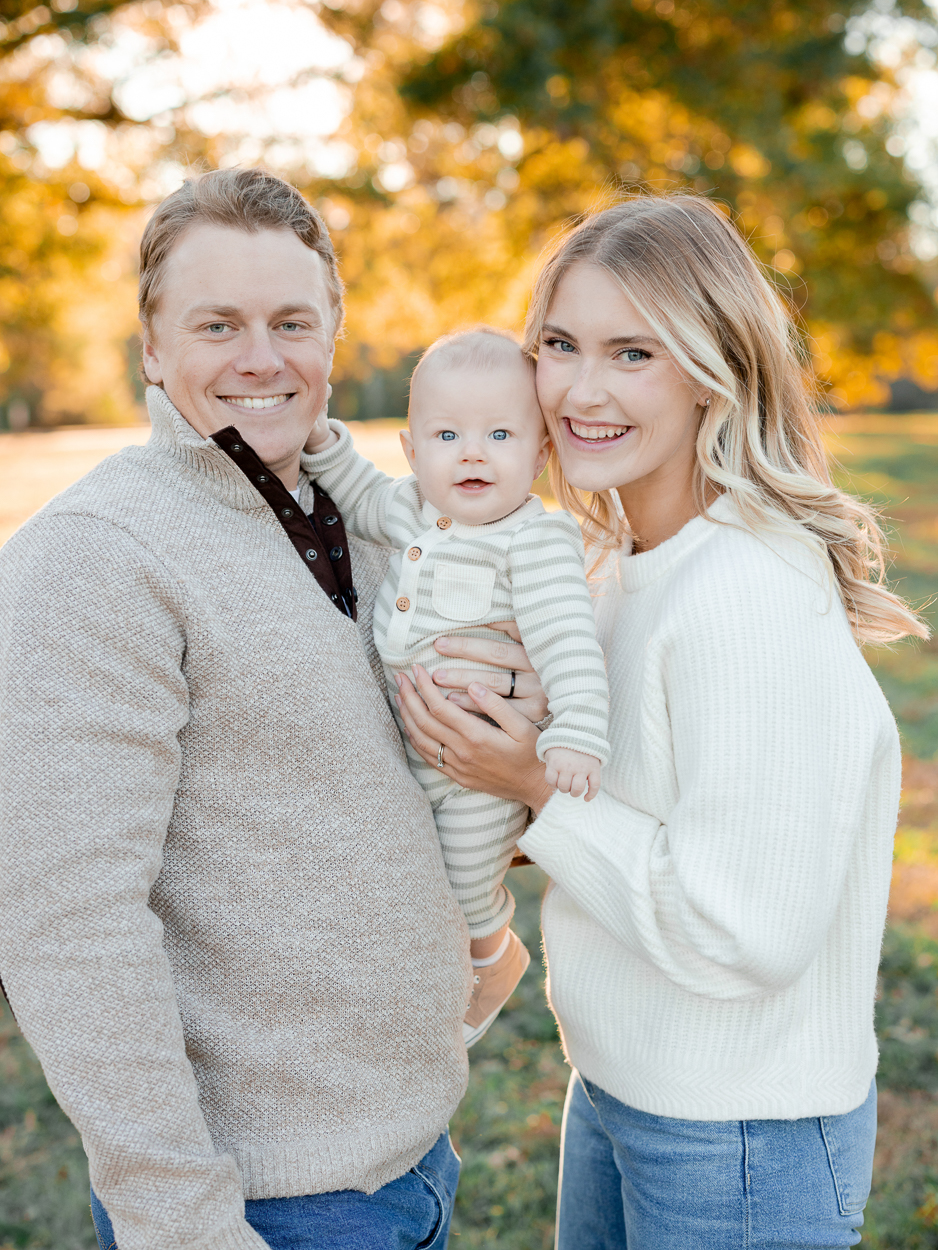 Parents holding their baby close and smiling at the camera with warm sunset light behind them, photographed by Love Tree Studios for golden sunset family photos in Columbia, MO.