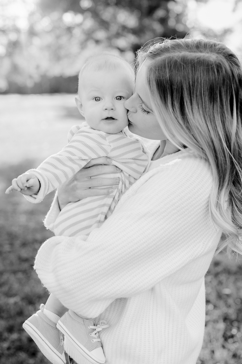 A mother holding her baby close and kissing his cheek in soft black and white light, photographed by Love Tree Studios for golden sunset family photos in Columbia, MO.