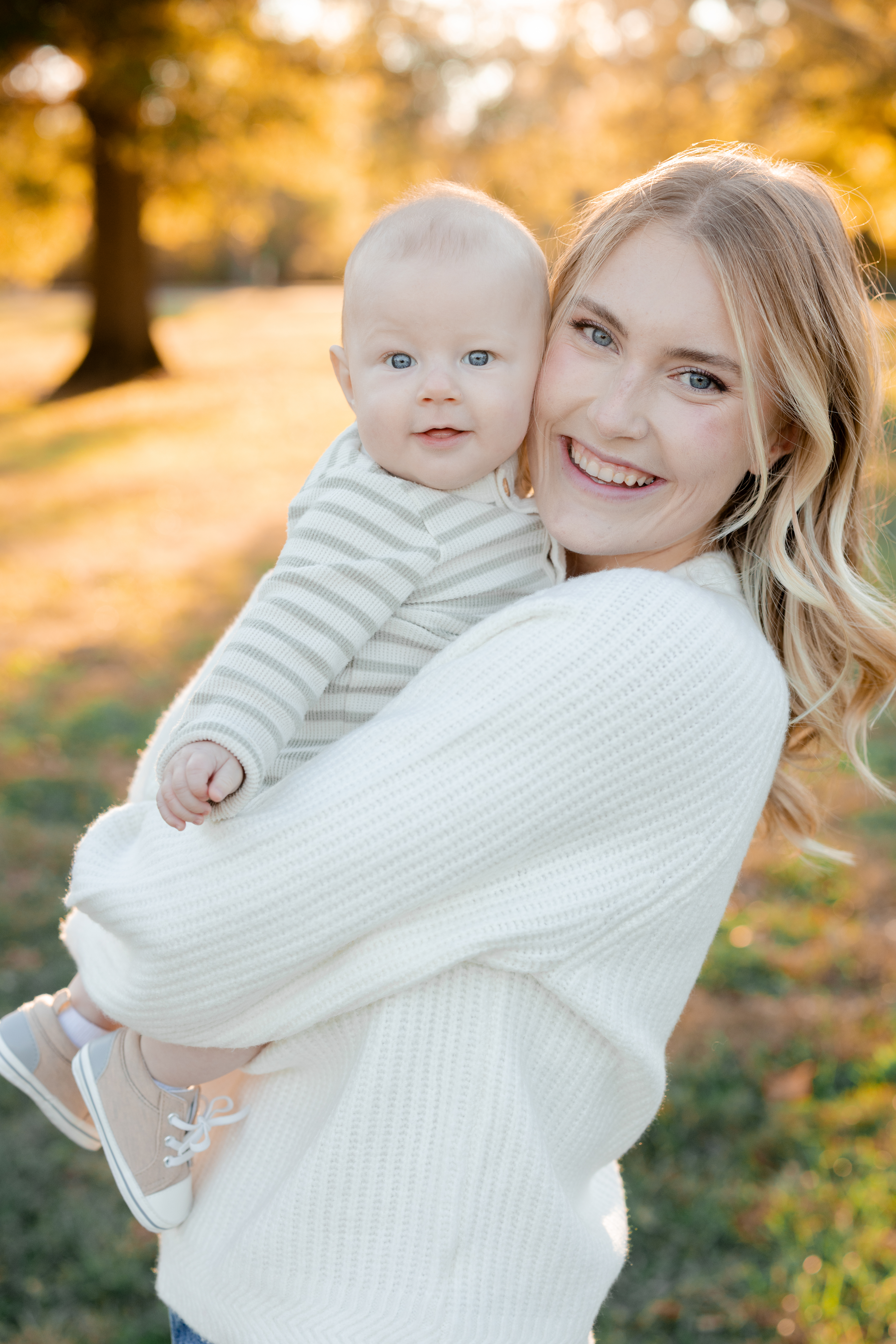 A mother smiling while holding her baby against a glowing fall backdrop, photographed by Love Tree Studios for golden sunset family photos in Columbia, MO.