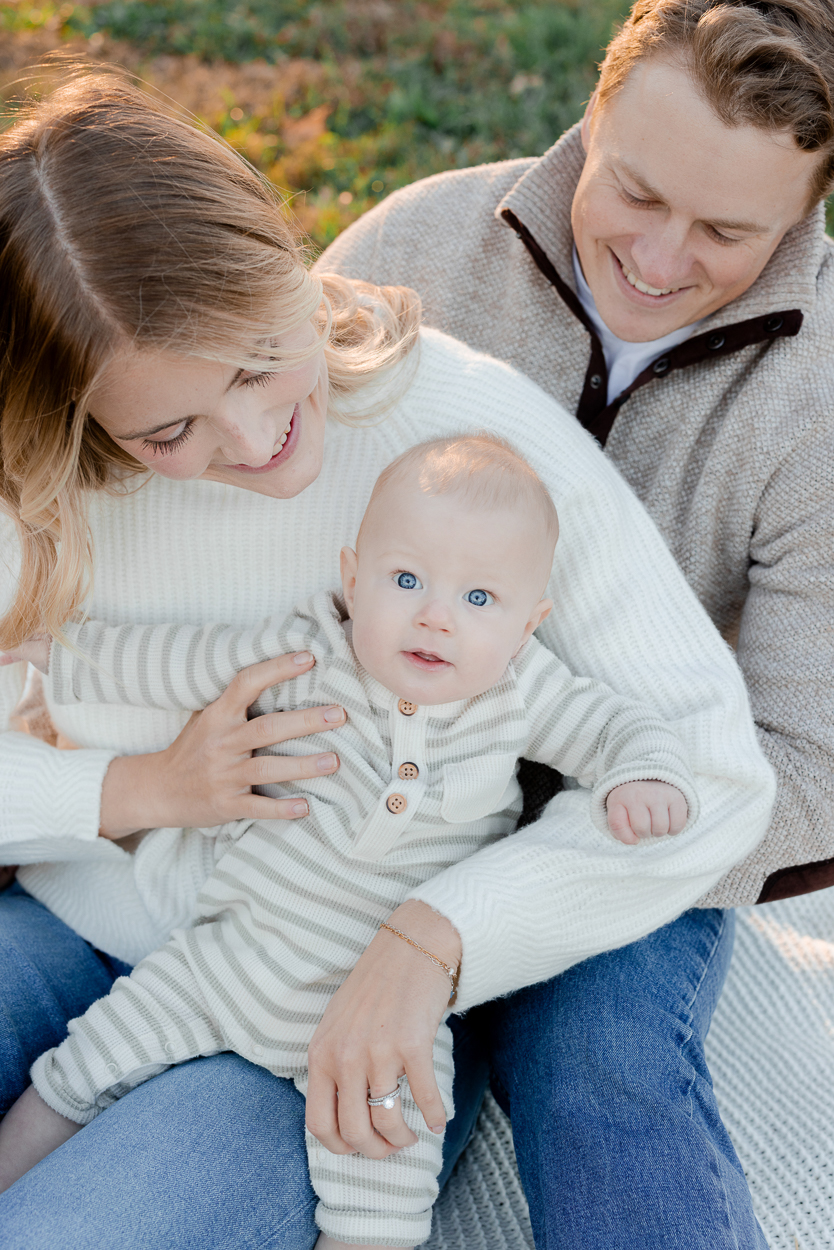 Parents sitting together and holding their baby while he looks up at the camera, captured by Love Tree Studios for golden sunset family photos in Columbia, MO.