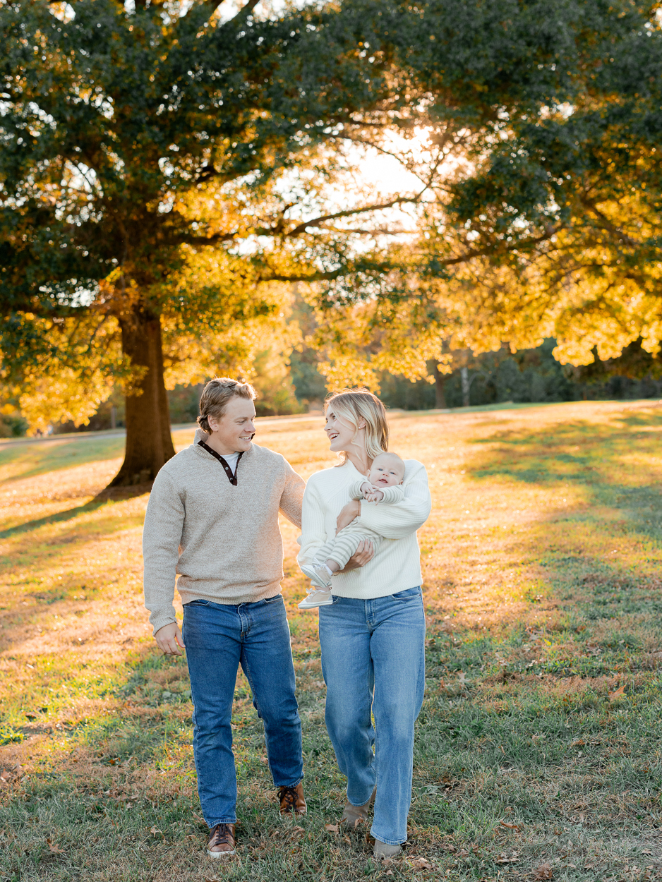 A family walking through a sunlit field with their baby in their arms, captured by Love Tree Studios for golden sunset family photos in Columbia, MO.