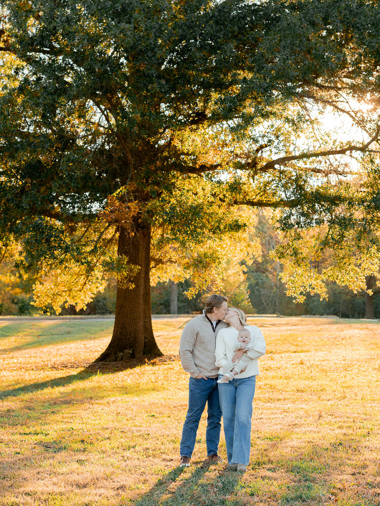 Parents lifting their baby into the air while standing in a glowing fall field, captured by Love Tree Studios for golden sunset family photos in Columbia, MO.