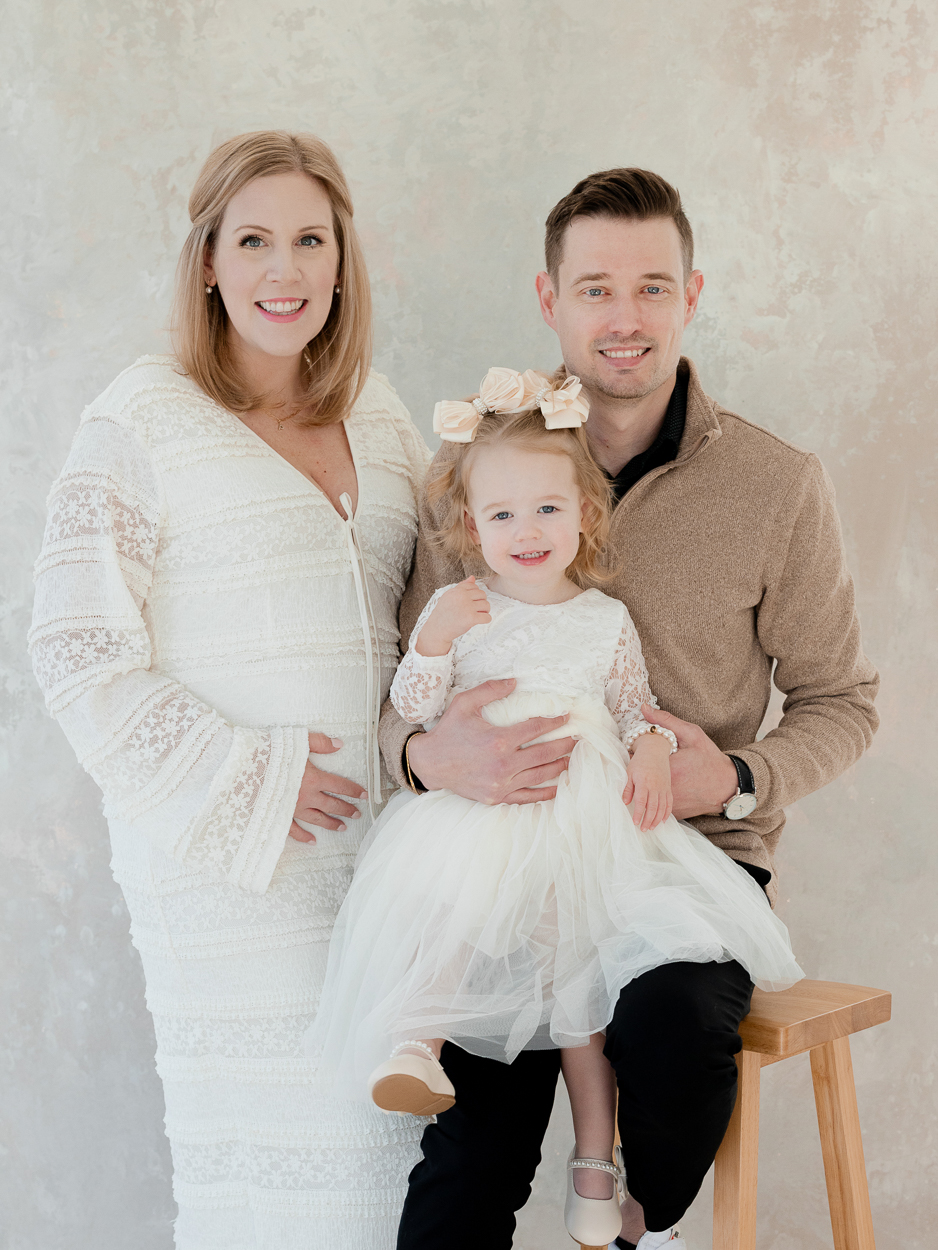Family portrait of mom, dad, and two year old daughter in soft neutral studio by Columbia Missouri family photographer.