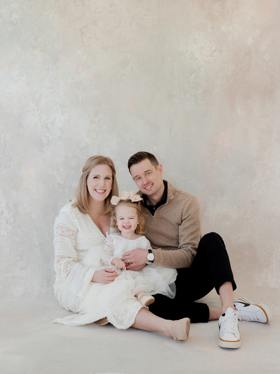 Smiling family of three seated on studio floor during Columbia Missouri family photography session
