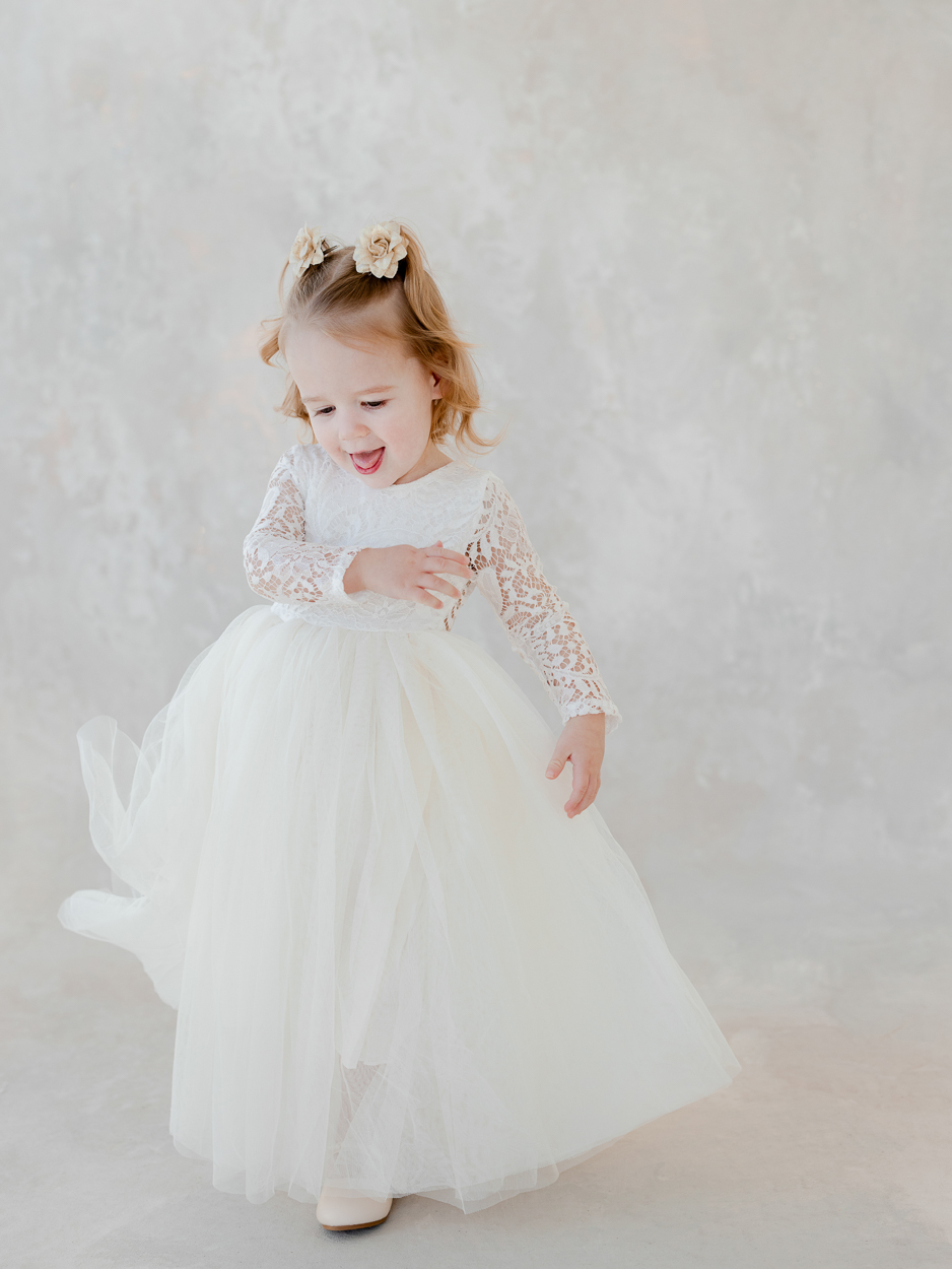 Two year old girl in white lace dress smiling during studio milestone session with Columbia Missouri family photographer.