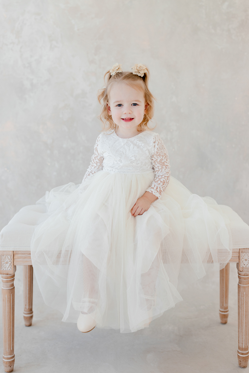 Two year old girl in white lace dress smiling during studio milestone session with Columbia Missouri family photographer.