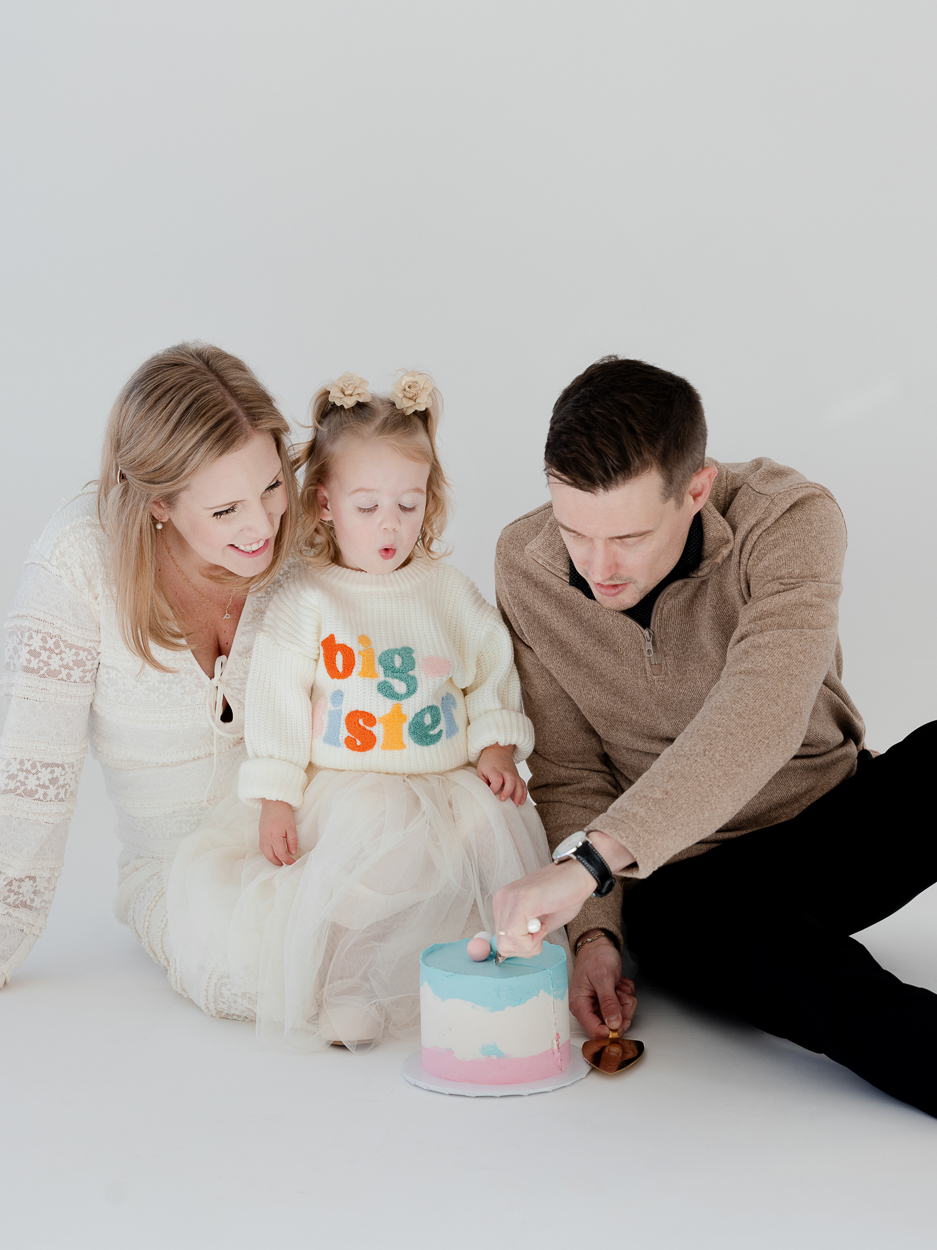 Parents and toddler reacting to cake reveal during Columbia Missouri studio family session.