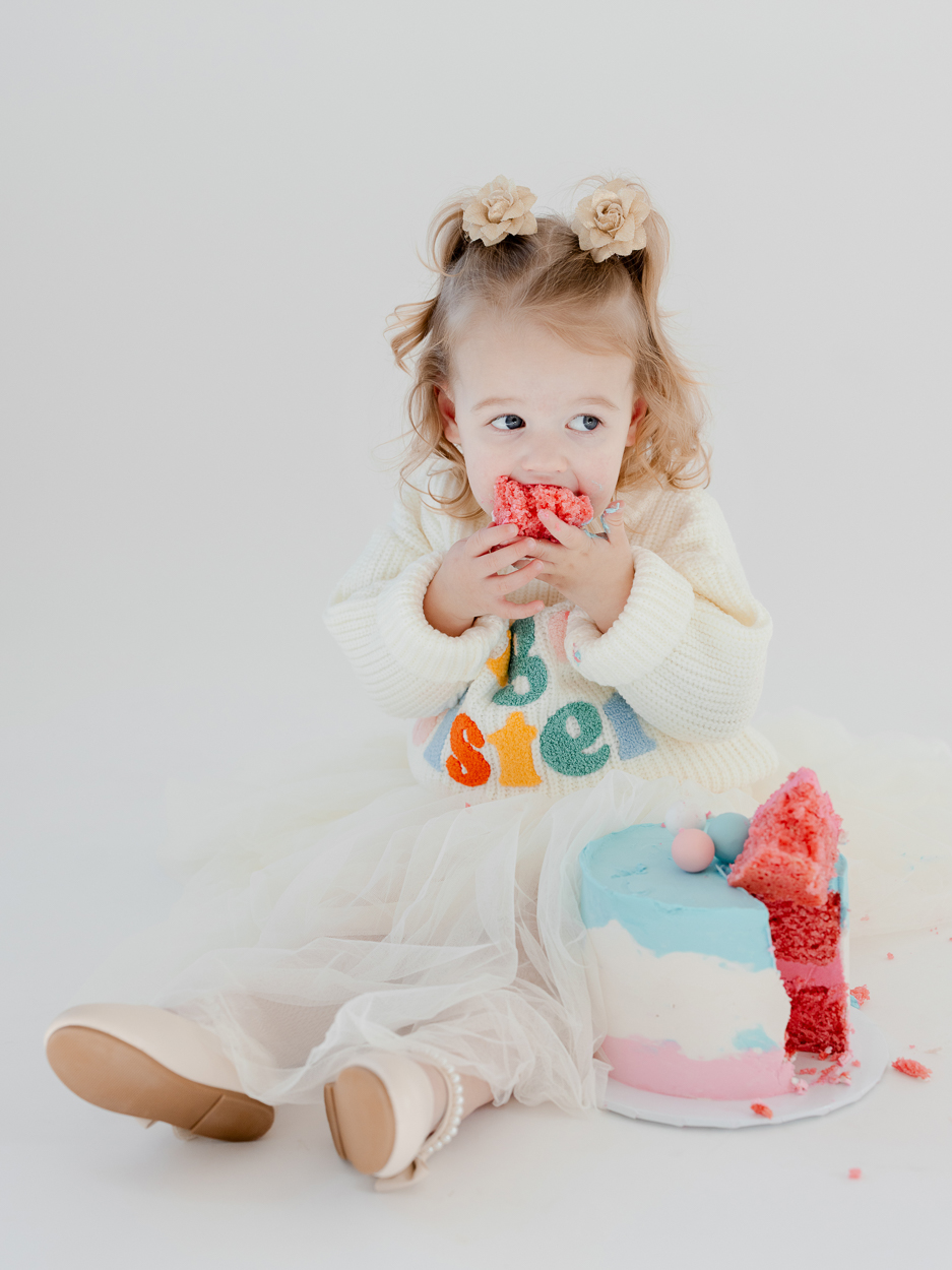 Toddler girl eating pink cake during studio birthday portrait session in Columbia Missouri.