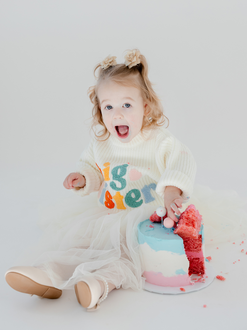 Two year old girl sitting on white studio floor with pastel cake during Columbia Missouri milestone session.