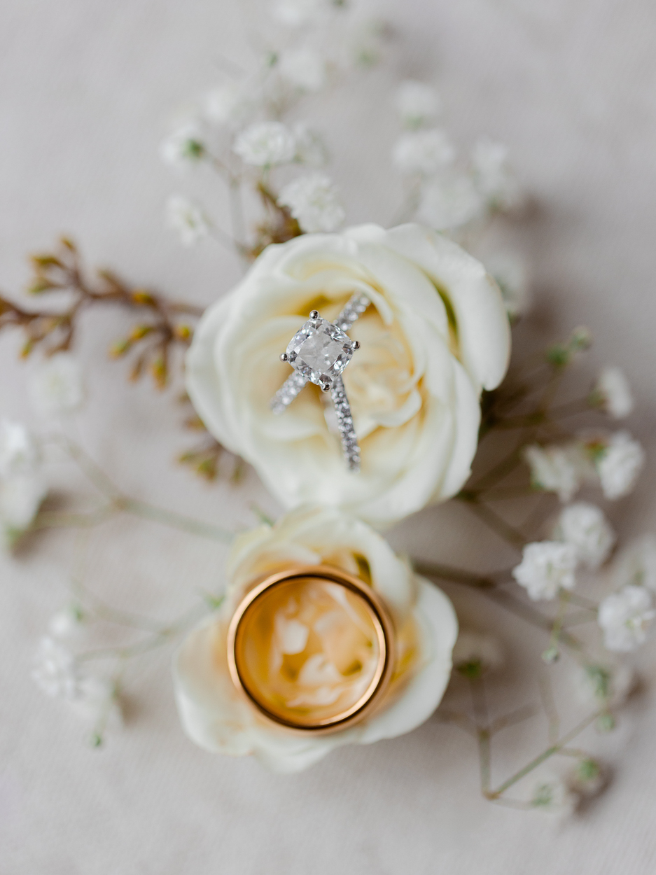 Detail photo of diamond engagement ring and gold wedding band styled on ivory rose at a Columbia Missouri church weddin