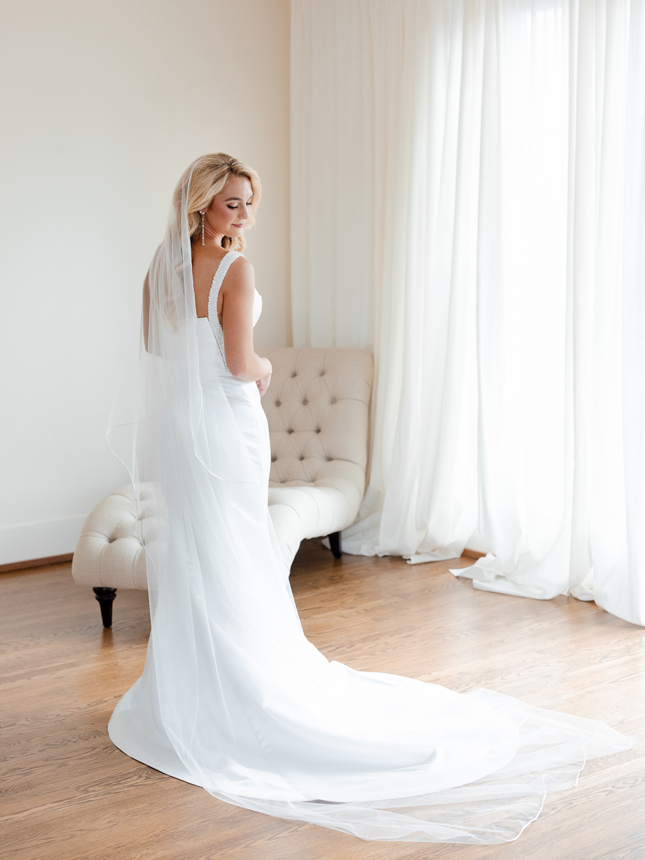 Full-length bridal portrait with long veil and fitted gown in natural window light before a Columbia Missouri church wedding.