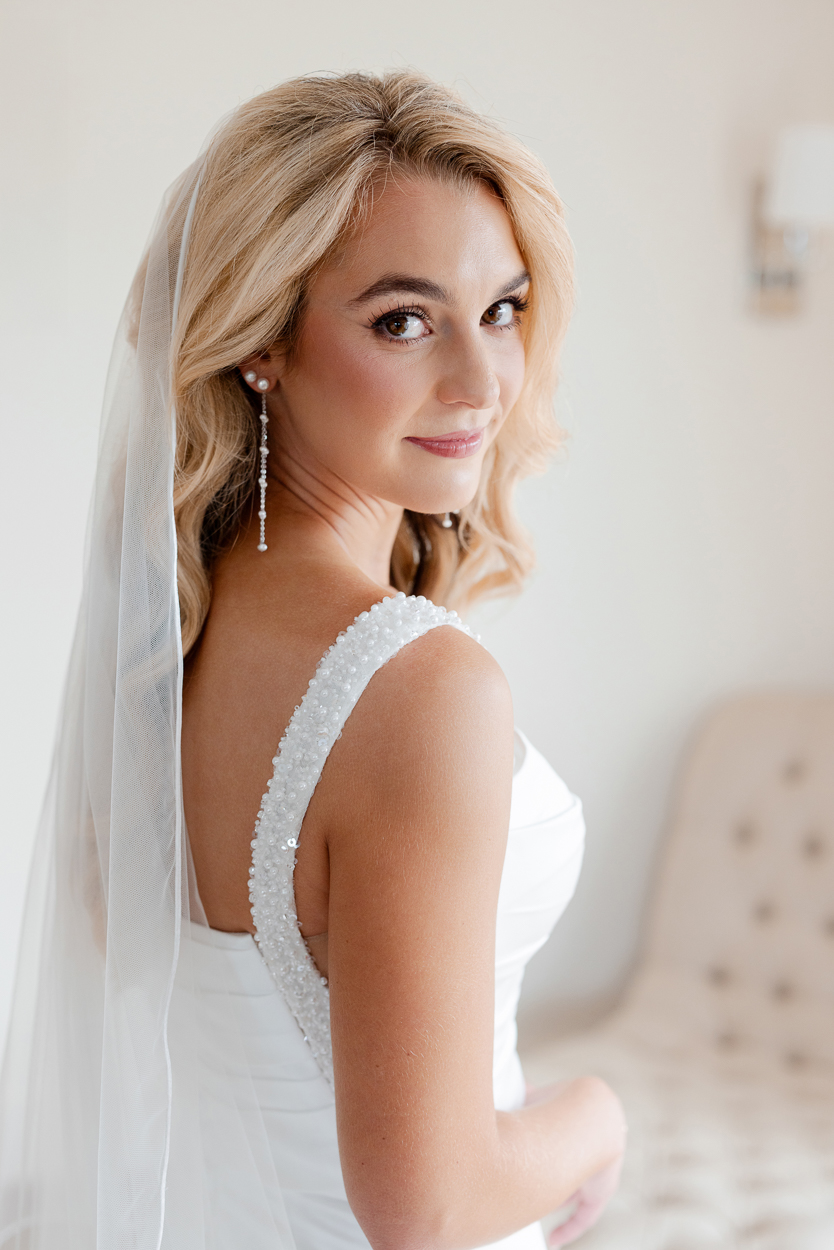Bride looking over her shoulder in soft window light with pearl straps and cathedral veil at a Columbia Missouri church wedding.