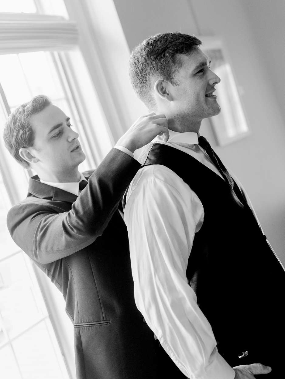 Groomsman helping the groom adjust his collar and vest in black and white before a Columbia Missouri church wedding.