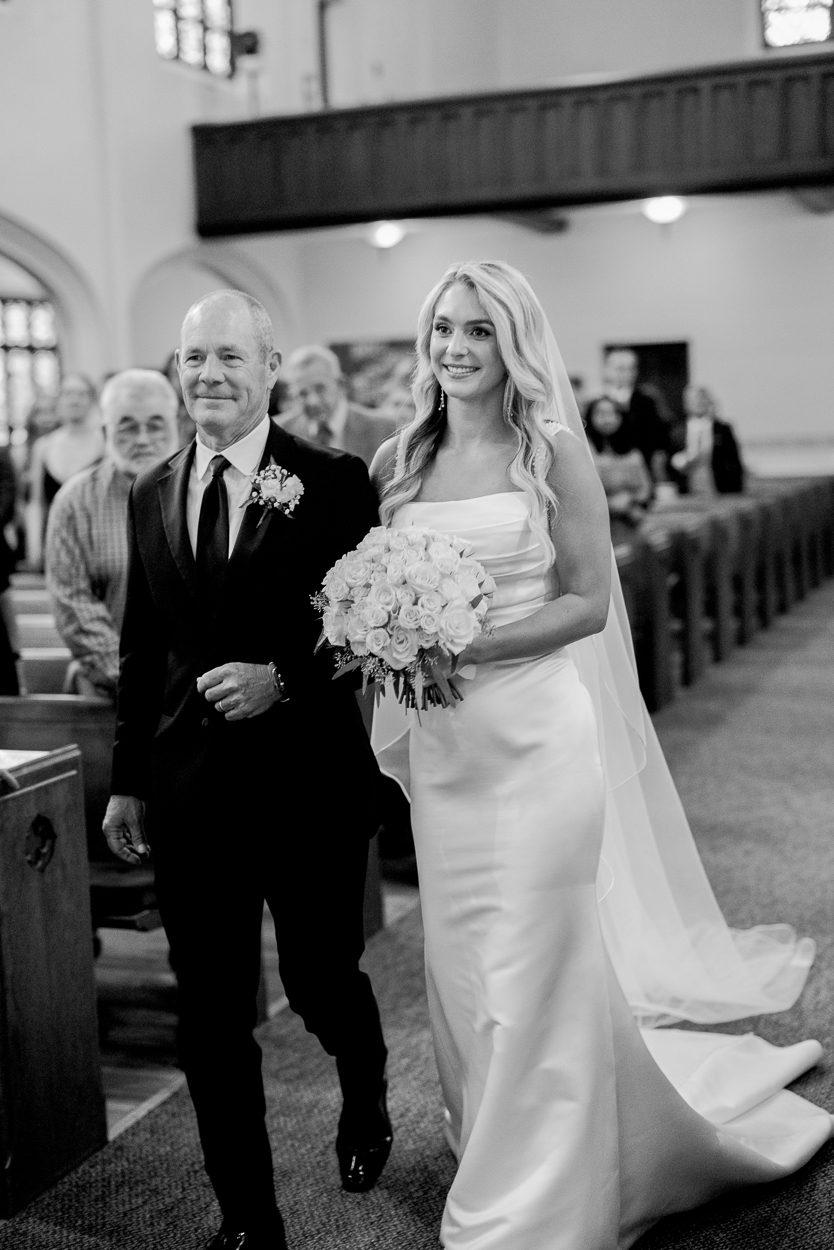 Bride walking down the aisle with her father holding a bouquet of white roses during a Columbia Missouri church wedding ceremony.