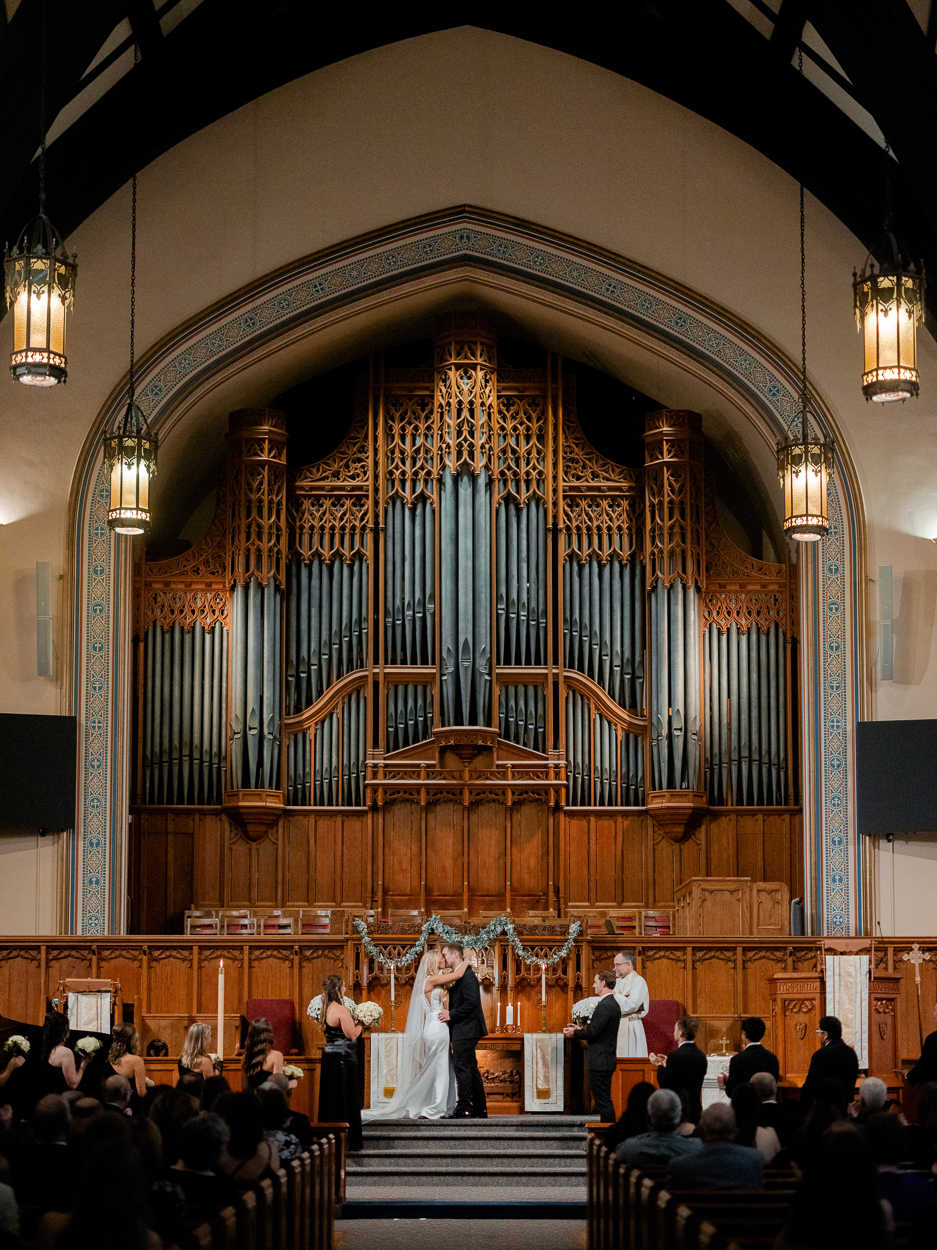 Newlyweds sharing their first kiss beneath the ornate church organ at a Columbia Missouri church wedding.