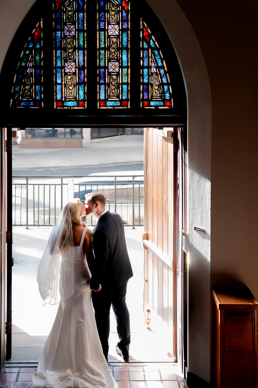 Newlyweds kissing in the doorway beneath stained glass windows after their Columbia Missouri church wedding.