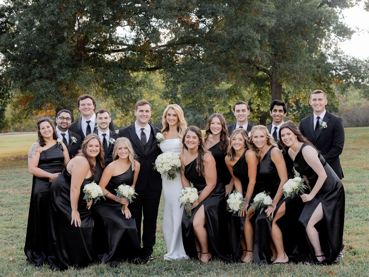 Bride and groom surrounded by bridesmaids and groomsmen in black attire at Stephens Lake Park in Columbia, Missouri.