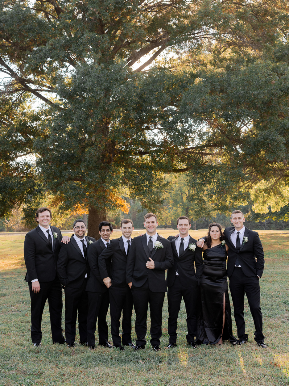 Groomsmen in black suits posing together beneath golden fall trees in Columbia, Missouri.