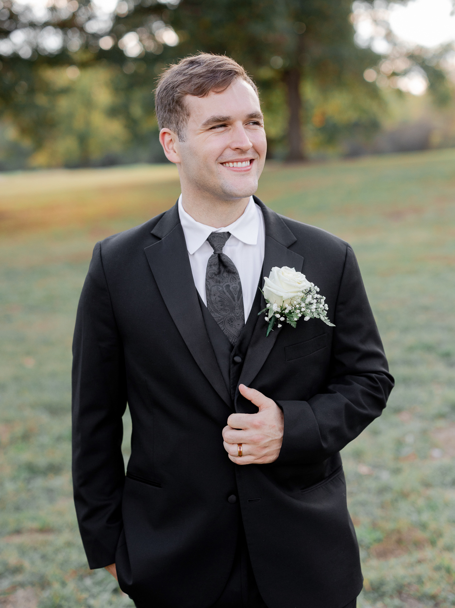 Groom portrait in a classic black suit with white rose boutonniere at Stephens Lake Park in Columbia, Missouri.