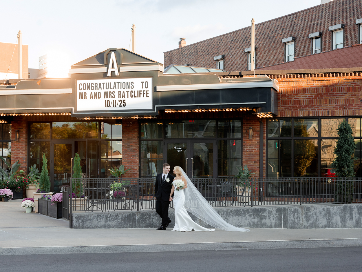 Newlyweds walking hand in hand beneath the marquee at The Atrium on Tenth in downtown Columbia, Missouri.