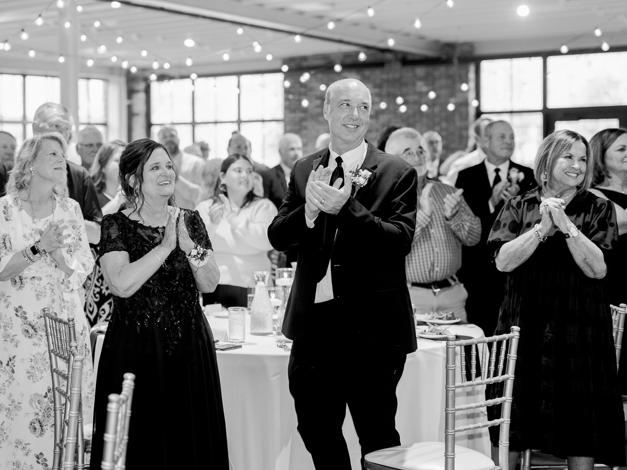 Wedding guests standing and applauding during the newlyweds’ reception entrance after a Columbia Missouri church wedding.