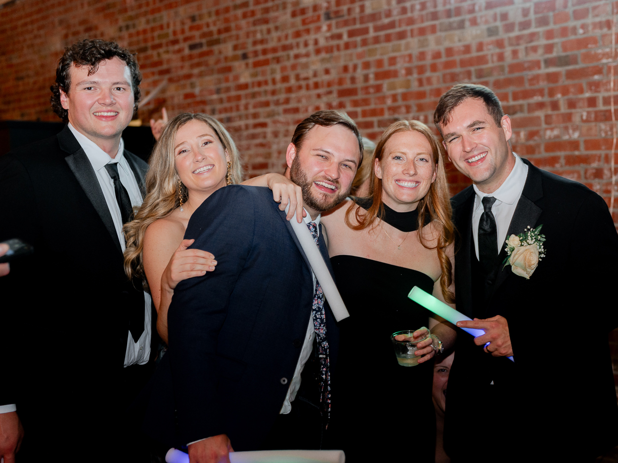 Group of friends posing together with drinks and glow sticks during a Columbia Missouri church wedding reception.
