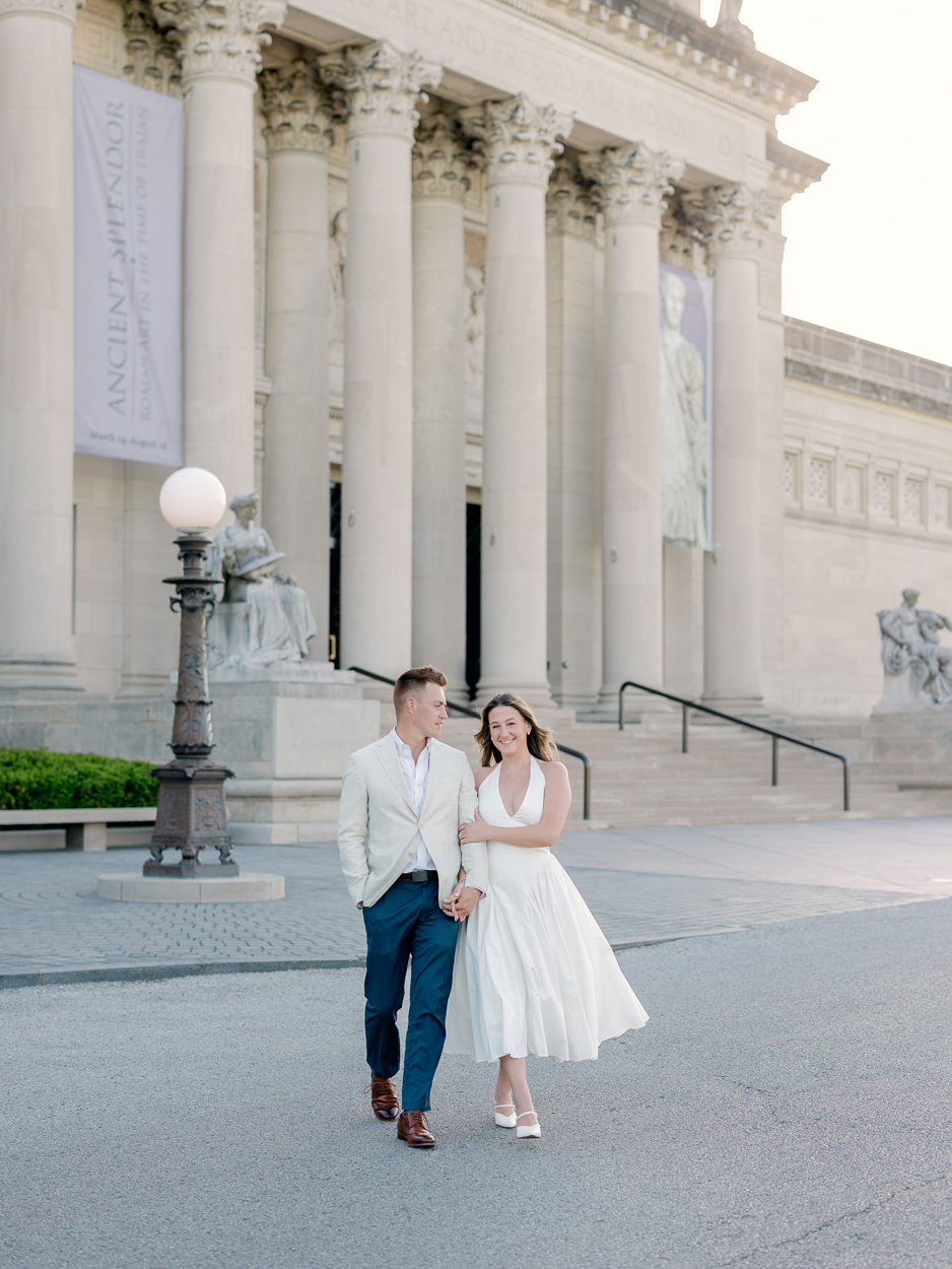 St. Louis engagement photographer captures couple walking hand in hand in front of the Saint Louis Art Museum at Art Hill in Forest Park.