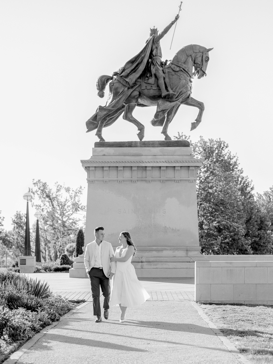 St. Louis engagement photographer captures couple walking in front of the Saint Louis statue monument at Art Hill in Forest Park in black and white.