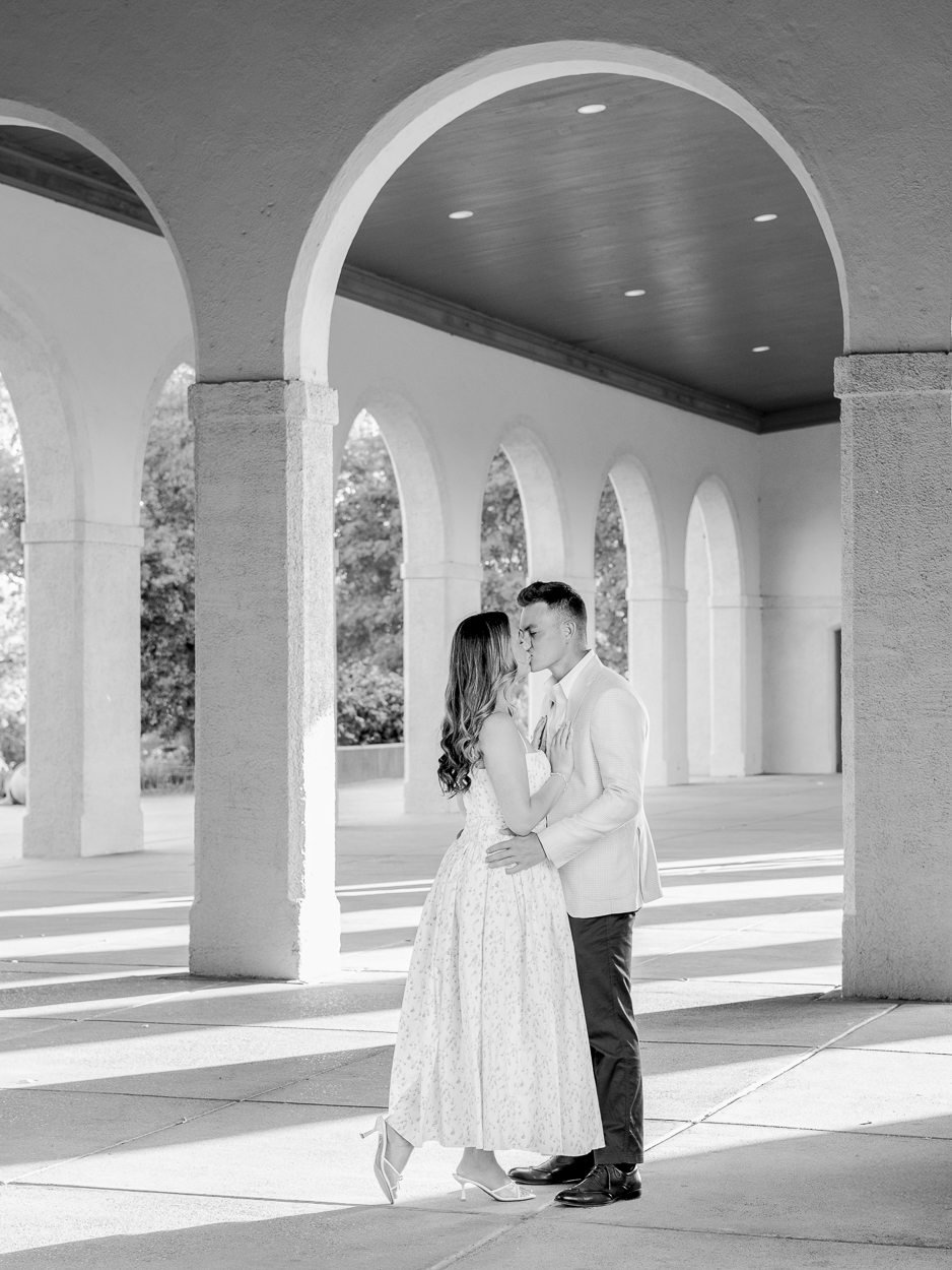 St. Louis engagement photographer captures couple kissing under the arched columns of the World's Fair Pavilion in Forest Park in black and white.