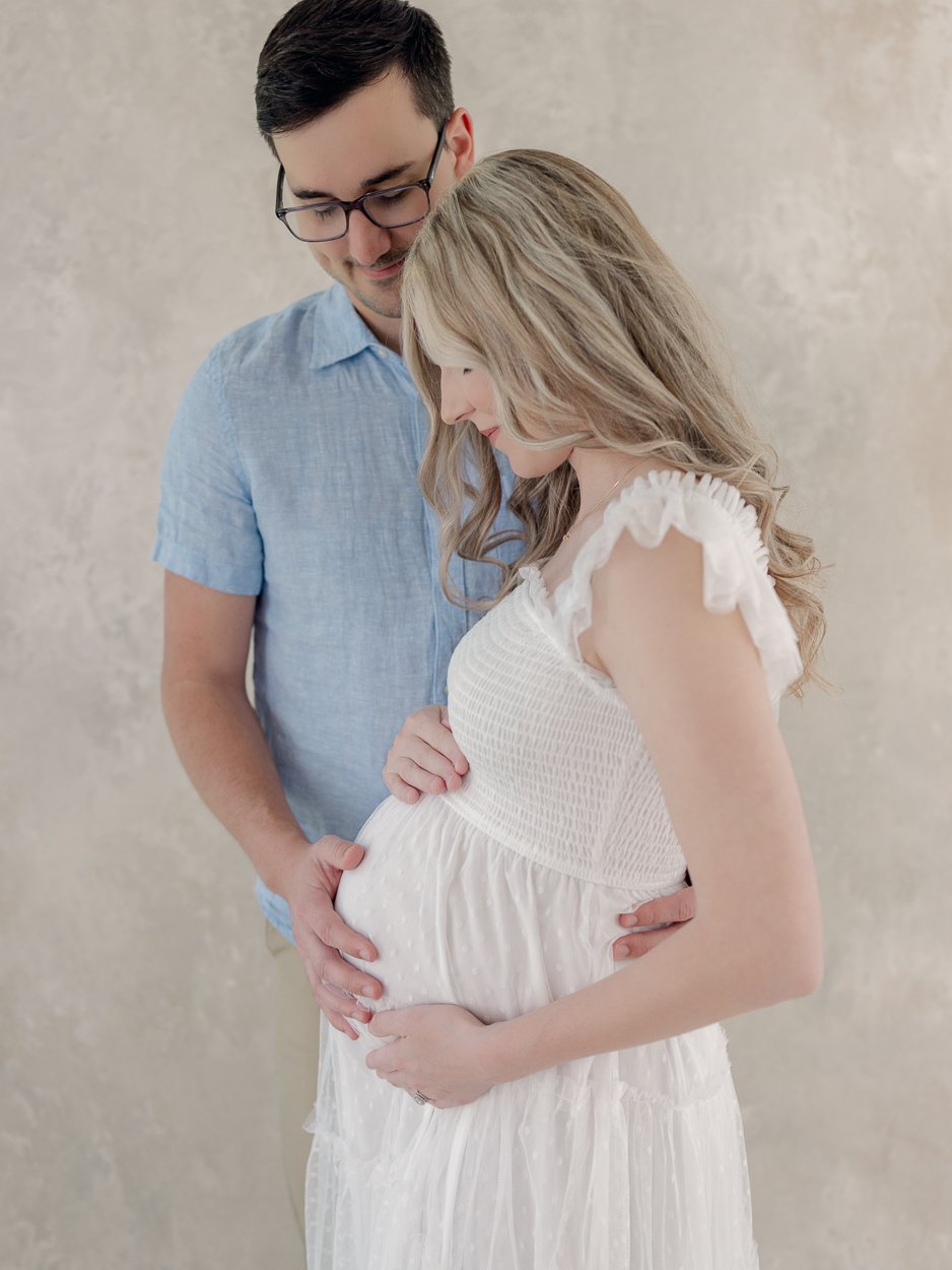 Close up of expecting couple's hands on pregnant belly with diamond engagement ring visible during maternity photography session at Love Tree Studios Columbia MO.