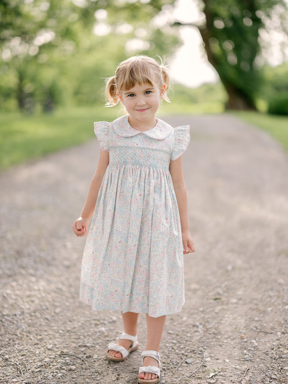 Little girl in floral dress and pigtails standing on a gravel driveway, Columbia Missouri family photographer.