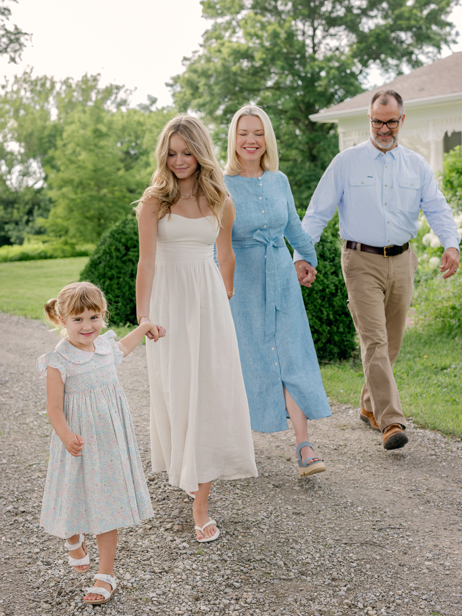 Family of four walking together in front of white Victorian farmhouse, Columbia MO family photographer