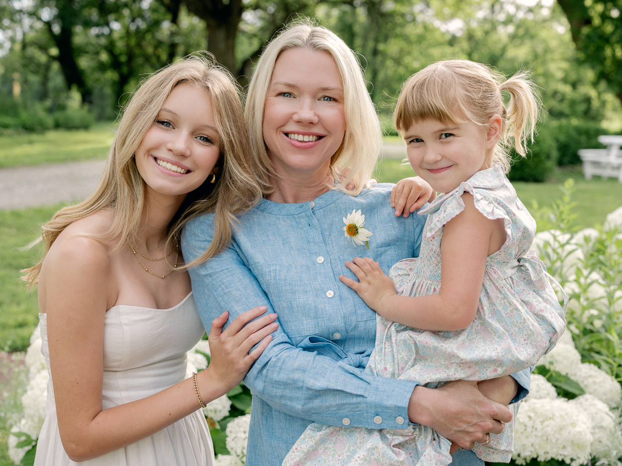 Three generations of women embracing, younger sister holding a daisy

