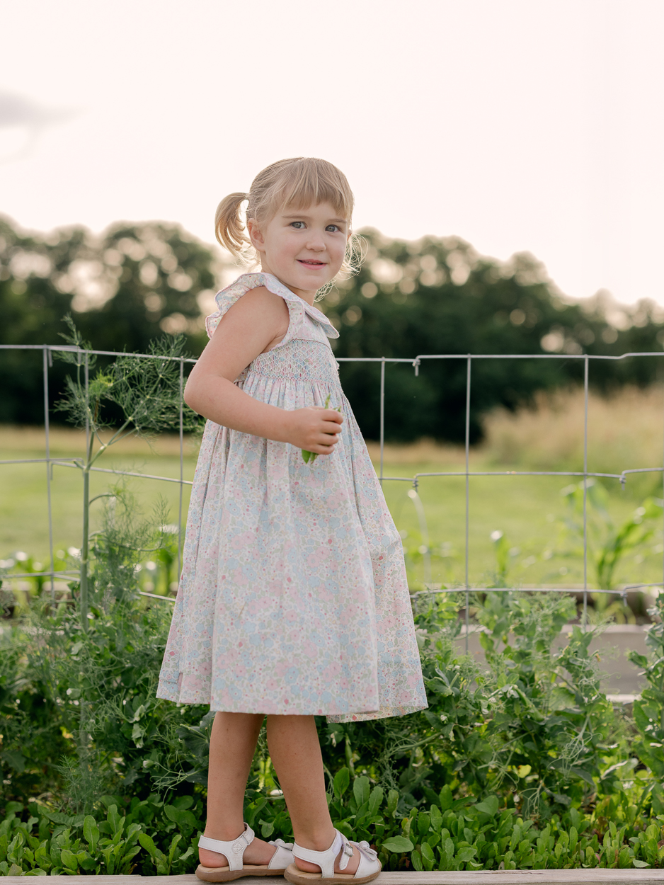 Little girl in garden holding a pea pod, side profile against a wire trellis.