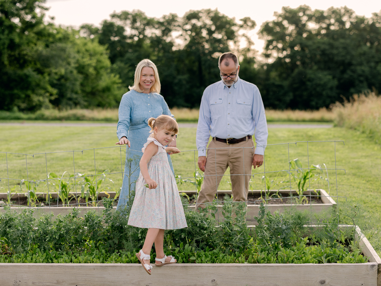 Little girl stepping along a garden bed edge while her parents watch and smile.