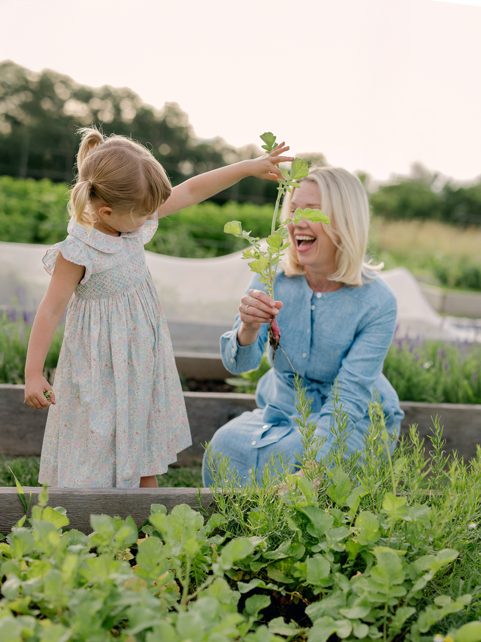 Mother laughing as her daughter hands her a freshly picked radish.