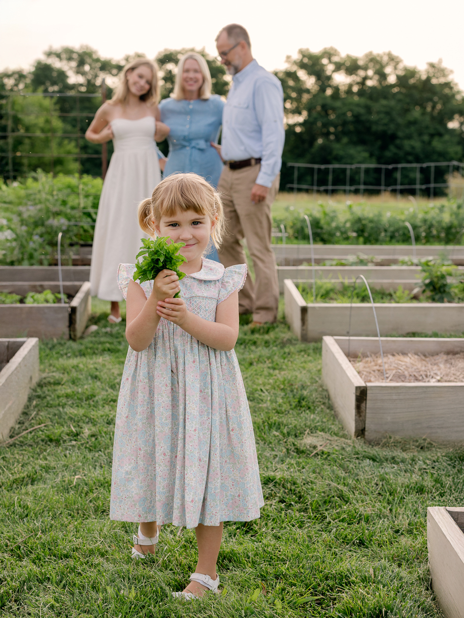Little girl holding a bundle of fresh herbs with her family blurred in the background.